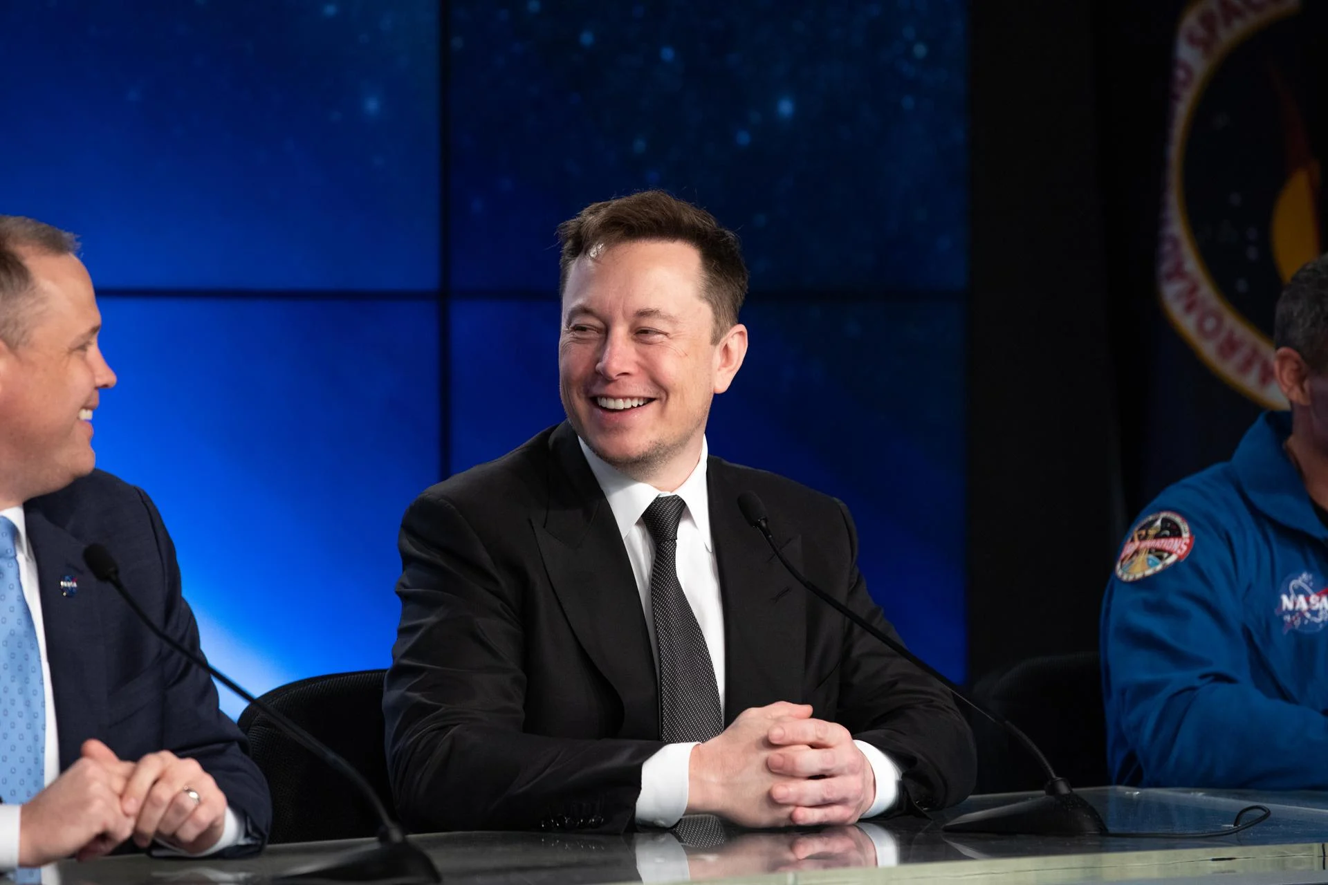 Elon Musk smiling at a NASA news conference, early life story